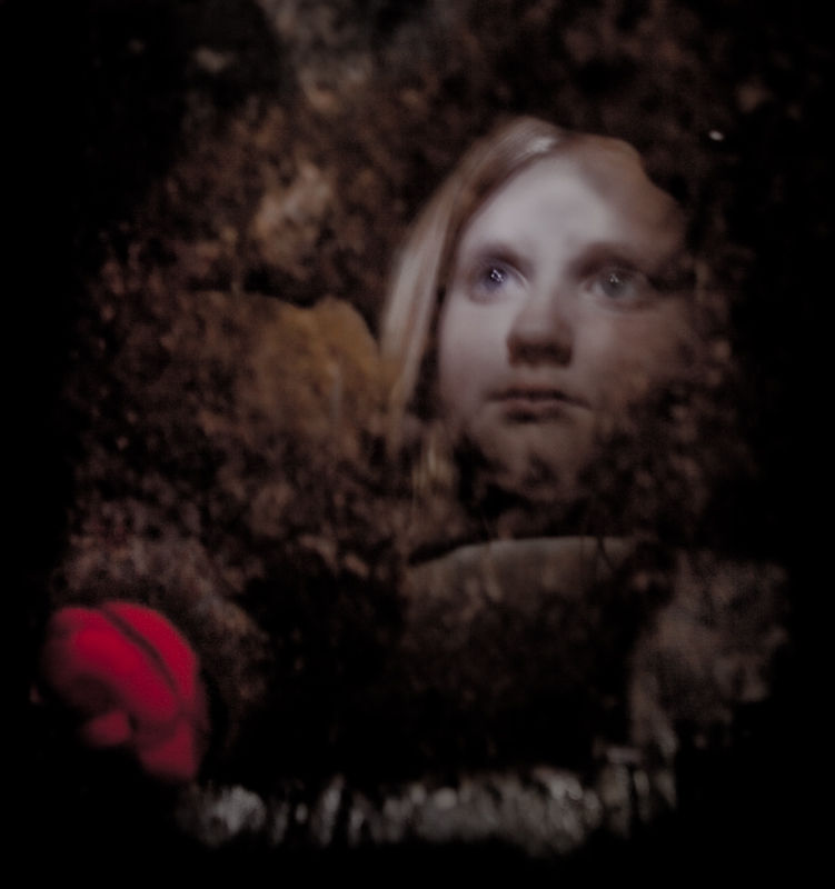 Eric’s daughter partly visible through layered dark textures with a red petal below